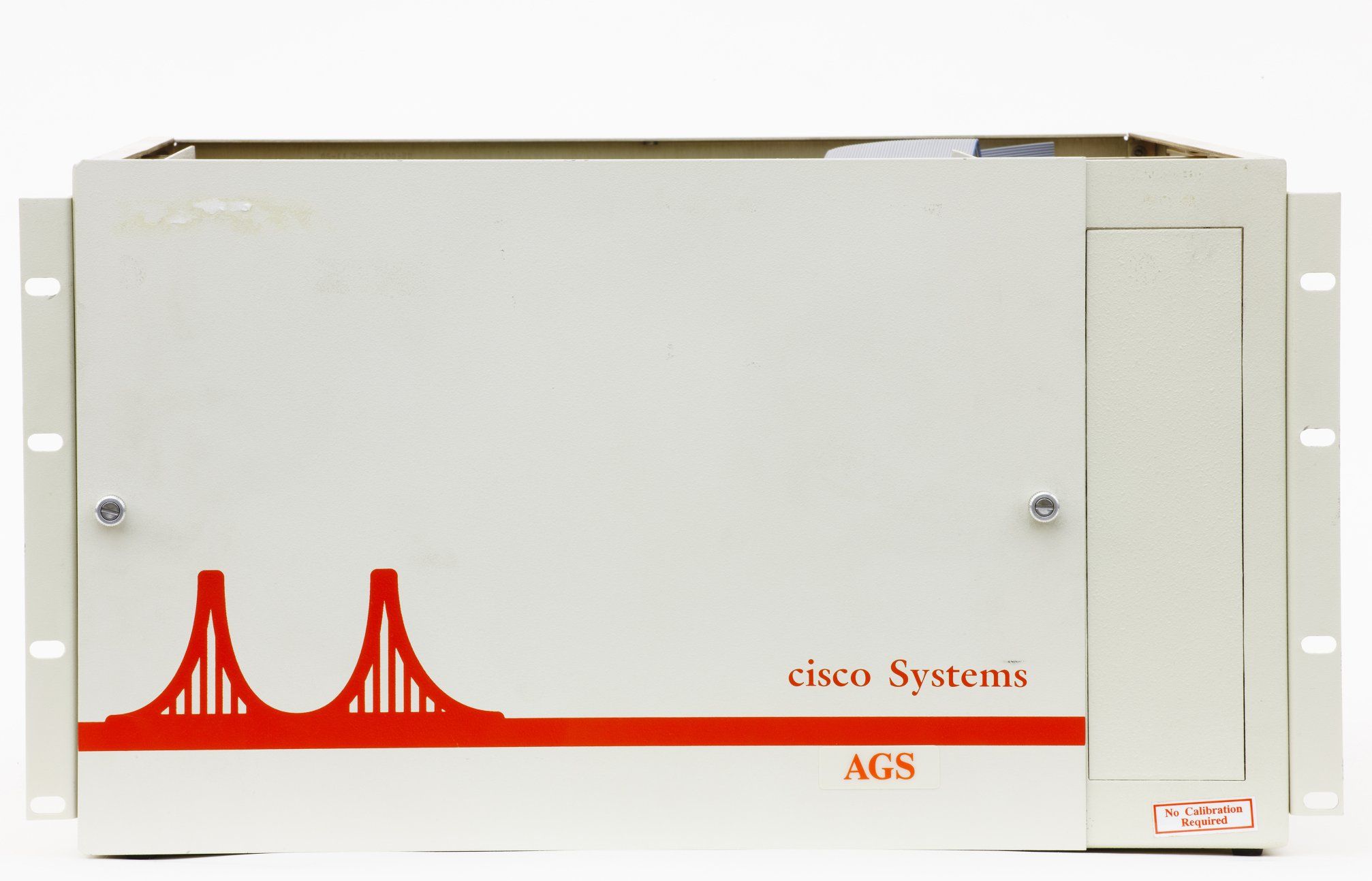 A front shot of the Cisco AGS chassis, a beige metal router with orange-red label in the shape of the first logo bridge and the company name