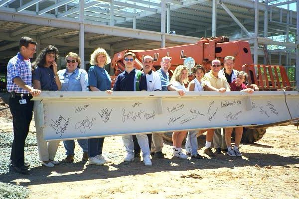 A group of employees stand behind a large construction beam covered in signatures at the RTP campus site