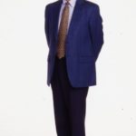 An executive headshot of Don Valentine, a white man in a blue suit with his hands behind his back
