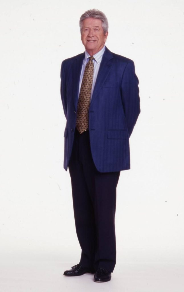An executive headshot of Don Valentine, a white man in a blue suit with his hands behind his back