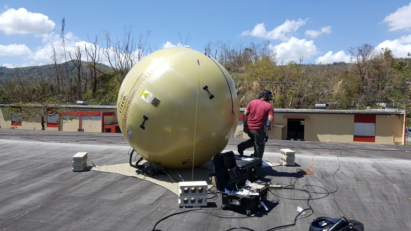 Man standing next to large satellite communications receiver on roof of building.
